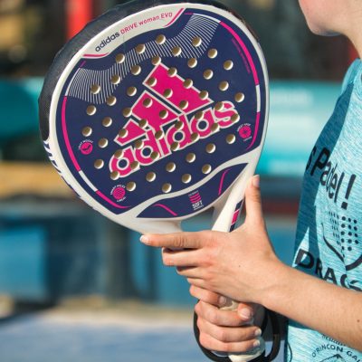Woman playing padel outdoors with Adidas racquet, showcasing sports equipment in action.